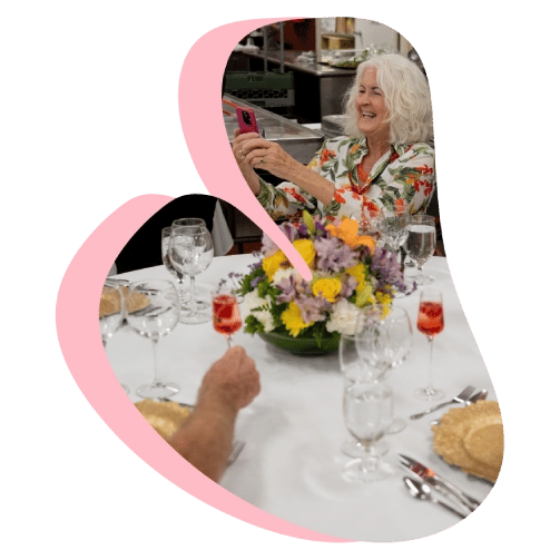 Person taking a photo with phone at a table set with flowers, drinks, and a festive centerpiece.