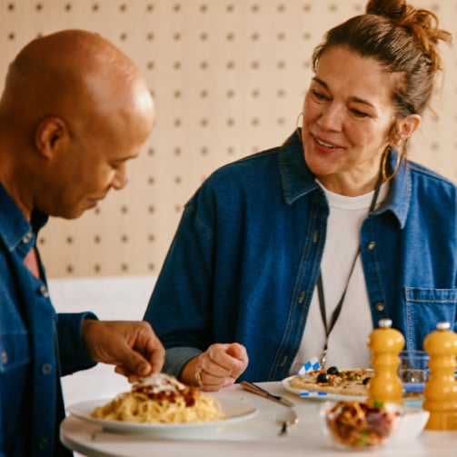 Two coworkers with blue t-shirts enjoying a pasta lunch together.