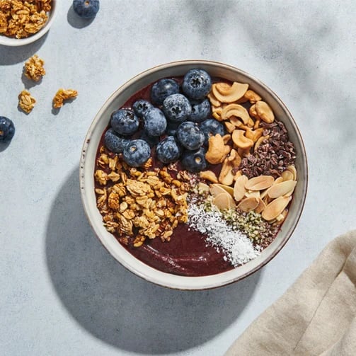 A bowl of acai topped with blueberries, cashews, granola, cacao nibs, sliced almonds, shredded coconut, and hemp seeds.