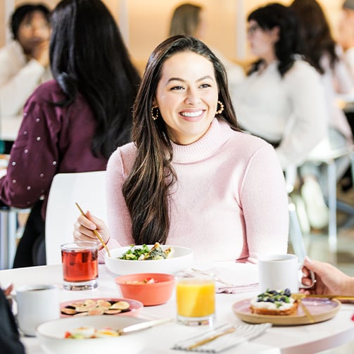 A woman seated at a table, enjoying a meal from a plate in front of her.