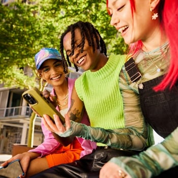 College students sitting outside together, laughing and engaging with a phone. 