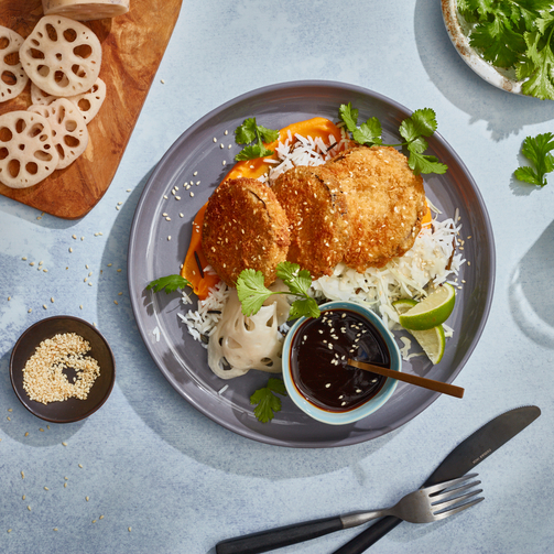 Overhead view of crispy breaded aubergine slices on rice with lotus root, herbs, lime, and dipping sauce.