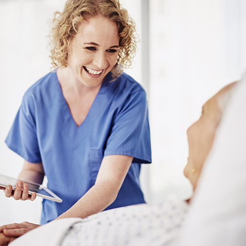A smiling nurse holding a tablet, checking in on a patient.