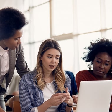 A professor guides two college students as they collaborate around a laptop.