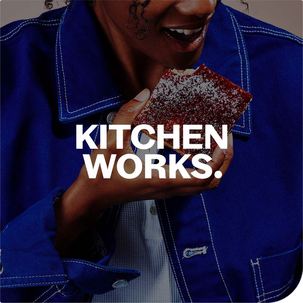 Person in blue jacket eating powdered pastry, with text "KITCHEN WORKS."