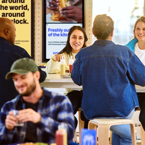 A busy eating area with people smiling while in conversation