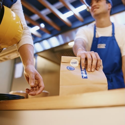 kitchen worker handing a lunch bag to customer