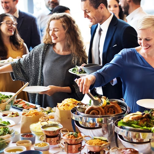 People serve themselves from a buffet table filled with salads, chips, and assorted dishes during a social gathering or event.