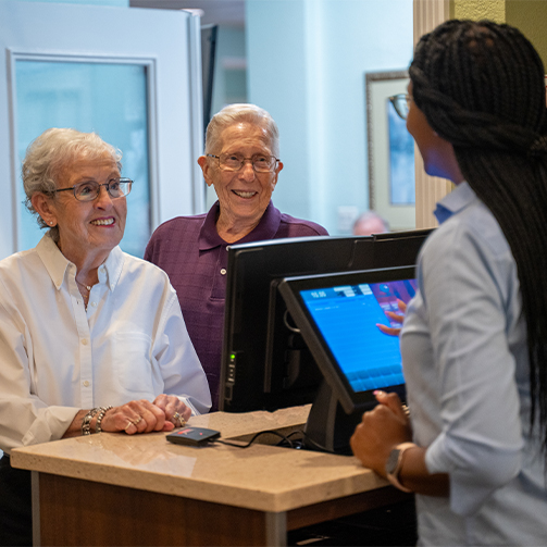 Senior resident couple smiling and chatting with a dining attendant.