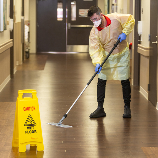 An environmental attendant wiping hospital floors with a single-use mop.