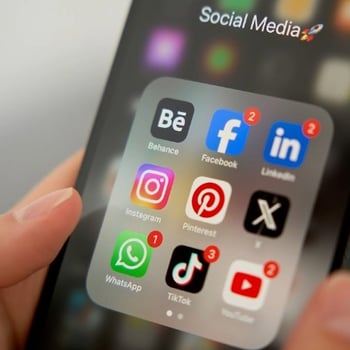 Close-up of a hand holding a smartphone displaying a folder of social media apps. 