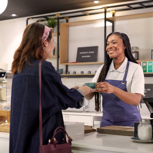 A smiling barista handing a cup of coffee to a customer at the counter.