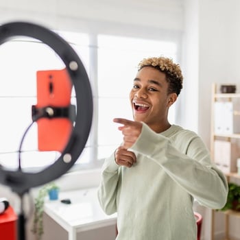 Student filming content with a smartphone and ring light in a bright room. 