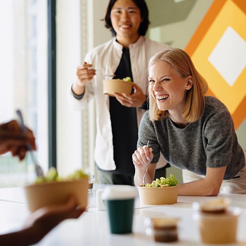 People eating salads at a table with vibrant geometric wall art in the background.
