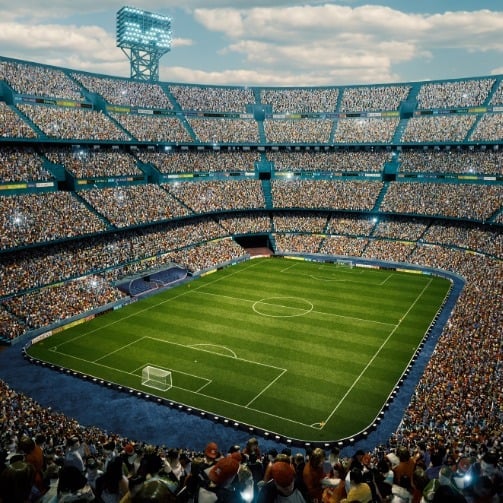 Aerial view of a large soccer stadium filled with spectators, featuring a green playing field at the center, surrounded by tiered seating and tall floodlights under a partly cloudy sky.