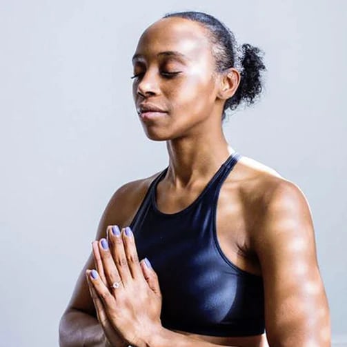 Person in a black sports bra with hands pressed together at chest in a yoga pose.