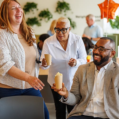 Group of people in a social setting with orange star-shaped balloons; one seated person holds a popcorn cup, another stands nearby also holding a cup.