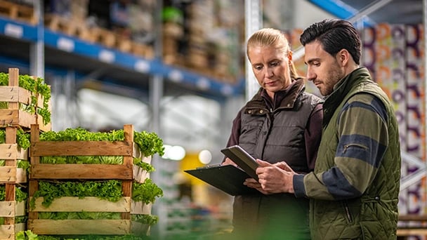 Two individuals examining a tablet together inside a warehouse setting.