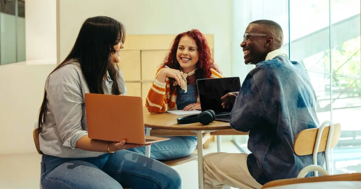 Group of college students collaborating at a round table with laptops in a well-lit room.
