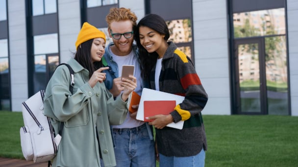 Friends huddled together, smiling and looking at a phone together.