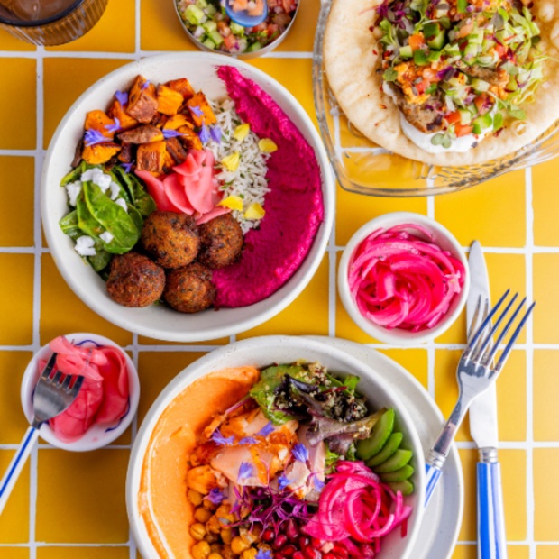A vibrant image featuring Greek-inspired bowl dishes with falafel, hummus, pickled onions and more.