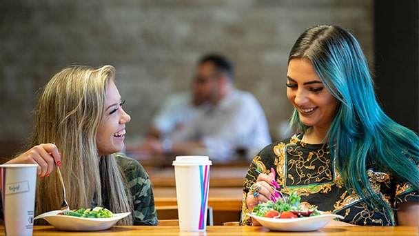 Two women enjoying salads at a restaurant table, engaged in conversation and smiling.