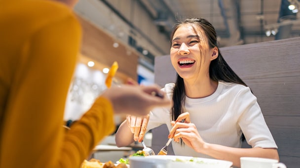 A woman enjoys a meal while seated at a table, focusing on her food with a content expression.