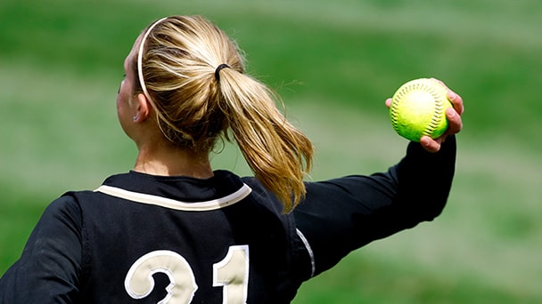 A female softball player in action, throwing a ball with focus and determination on a sunny field.