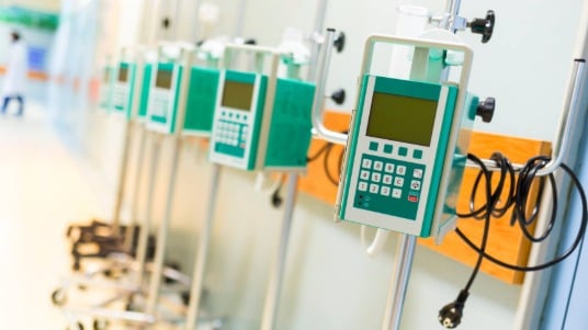 A row of infusion pumps lined up standing in a hospital corridor.