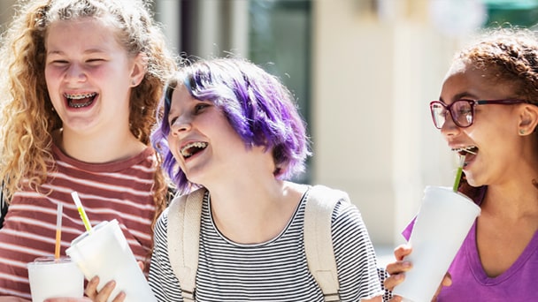 Three girls laughing together while holding drinks, enjoying a cheerful moment.
