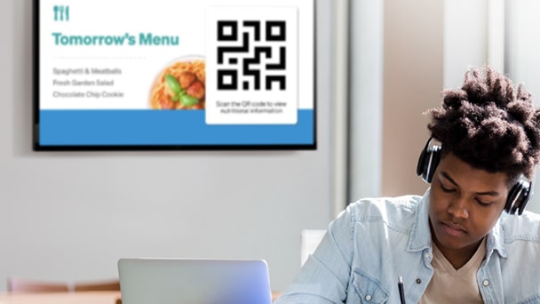 A man sitting at a table with a laptop and a QR code displayed on the surface.