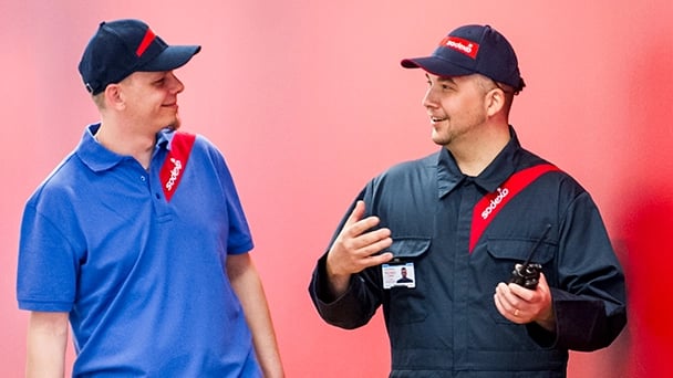 Two men wearing blue and red uniforms stand together, smiling in a friendly manner.