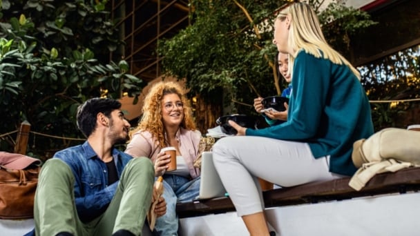Group of college students sitting together in a courtyard, enjoying lunch.