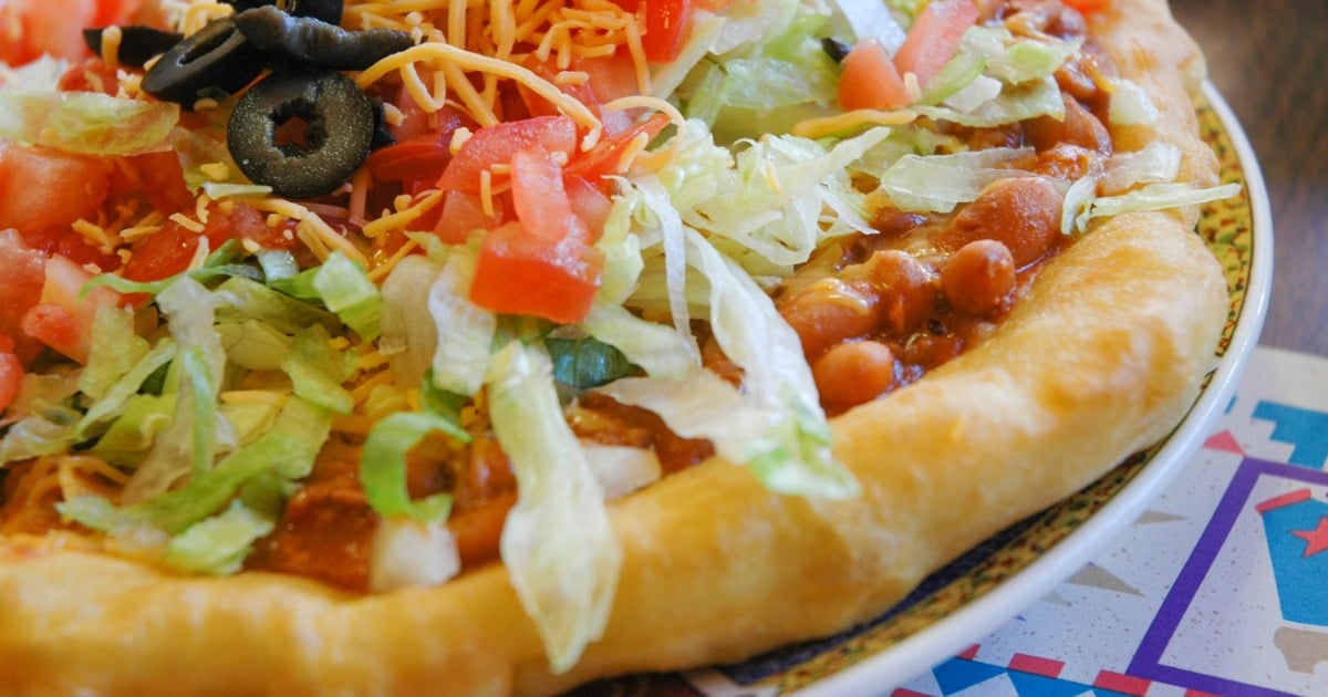 Close-up shot of a NDN taco, a traditional Native American frybread topped with beans, cheese, lettuce and tomato. 