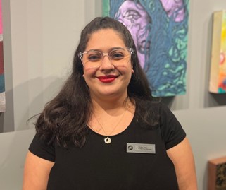 Person in black shirt with name tag standing before colorful abstract paintings on a wall.