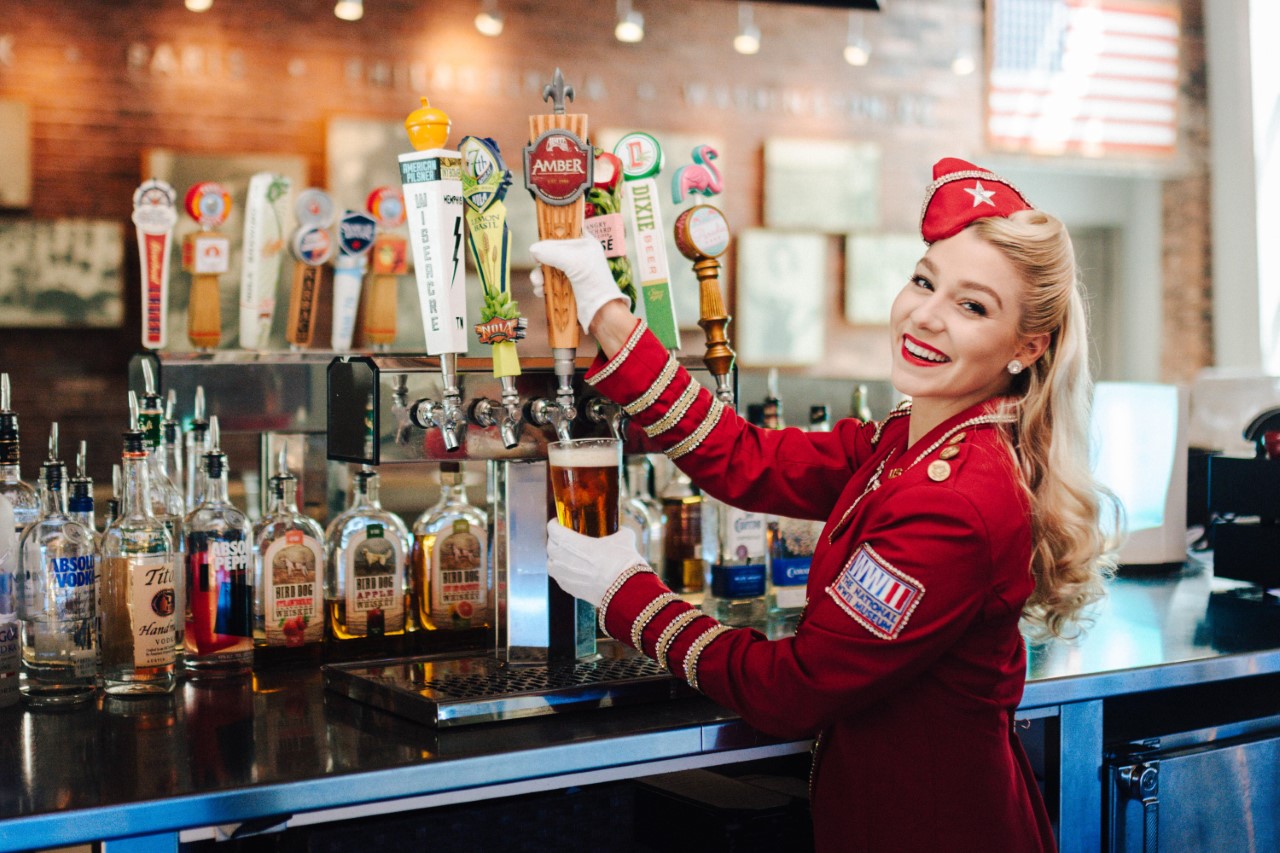 blond girl with WWII red uniform filling a glass with beer