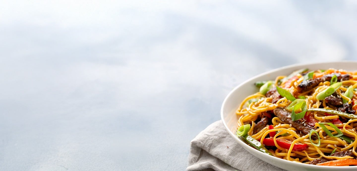 Close-up of an Asian-inspired beef stir-fry noodle bowl with vegetables and sprinkled sesame seeds. 