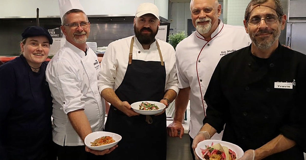 Chef Efrén Hernández with SUNY chefs presenting plated dishes in a campus kitchen. 