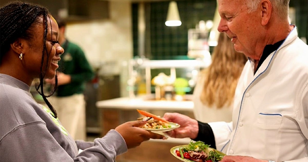 Chef personally serving a salad dish to a student in a campus dining hall. 