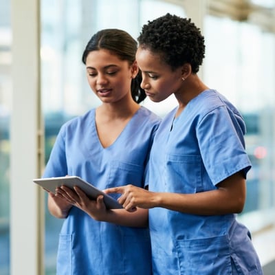 Two dietetics professionals in blue scrubs looking at a tablet together. 