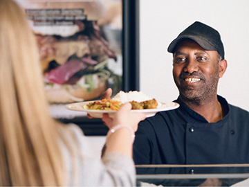 A dining employee serving food to a student.