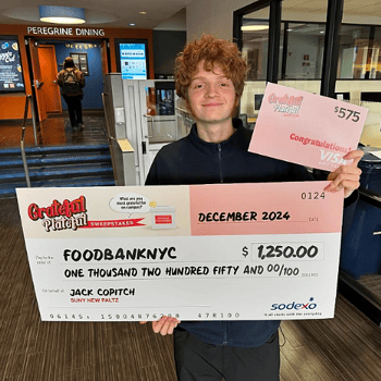 SUNY New Paltz student holding up a giant check for $1,250 made out to FoodBank NYC. 