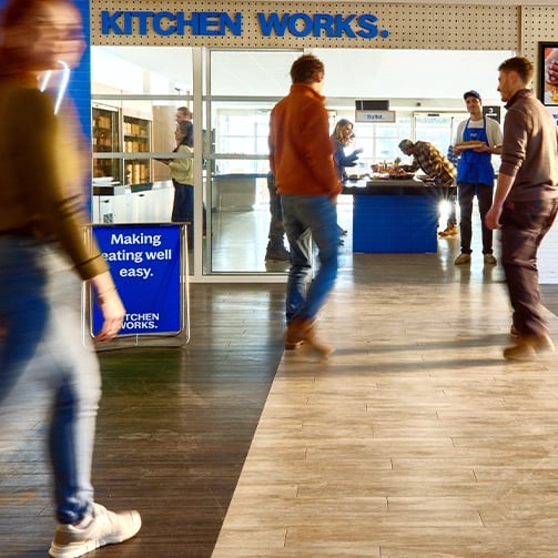 People outside a location called “KITCHEN WORKS” with a sign that says “Making eating well easy."