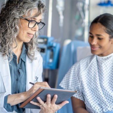 A registered dietitian sits beside a patient in a hospital bed, reviewing a nutrition plan together. 