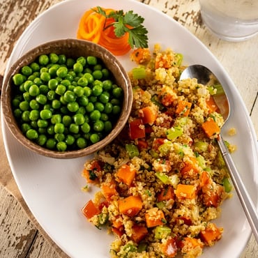 A plant-based quinoa primavera garnished with fresh herbs, served with a side of peas and a glass of water. 