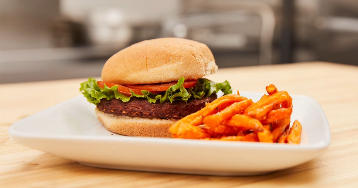 Plant-based school lunch option with a black bean burger and sweet potato fries on a plate. 