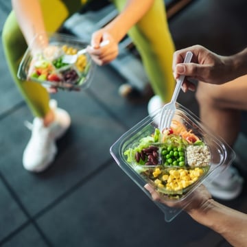 Two student-athletes enjoying fresh, nutritious salads together in a campus gym after a workout. 
