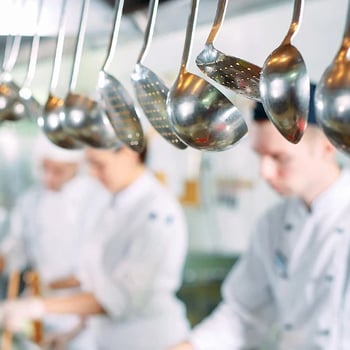 Hanging kitchen utensils in focus with chefs working in the background.  