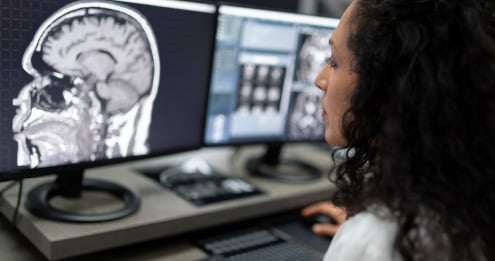 Person reviewing brain scan images on multiple computer monitors.