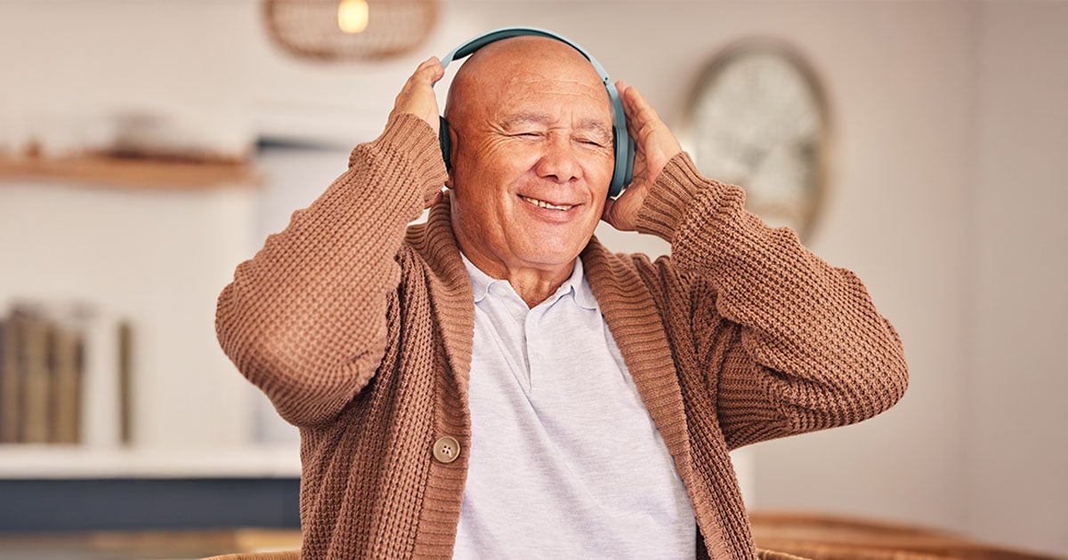 Senior man wearing headphones, eyes closed, smiling softly as he listens to music.